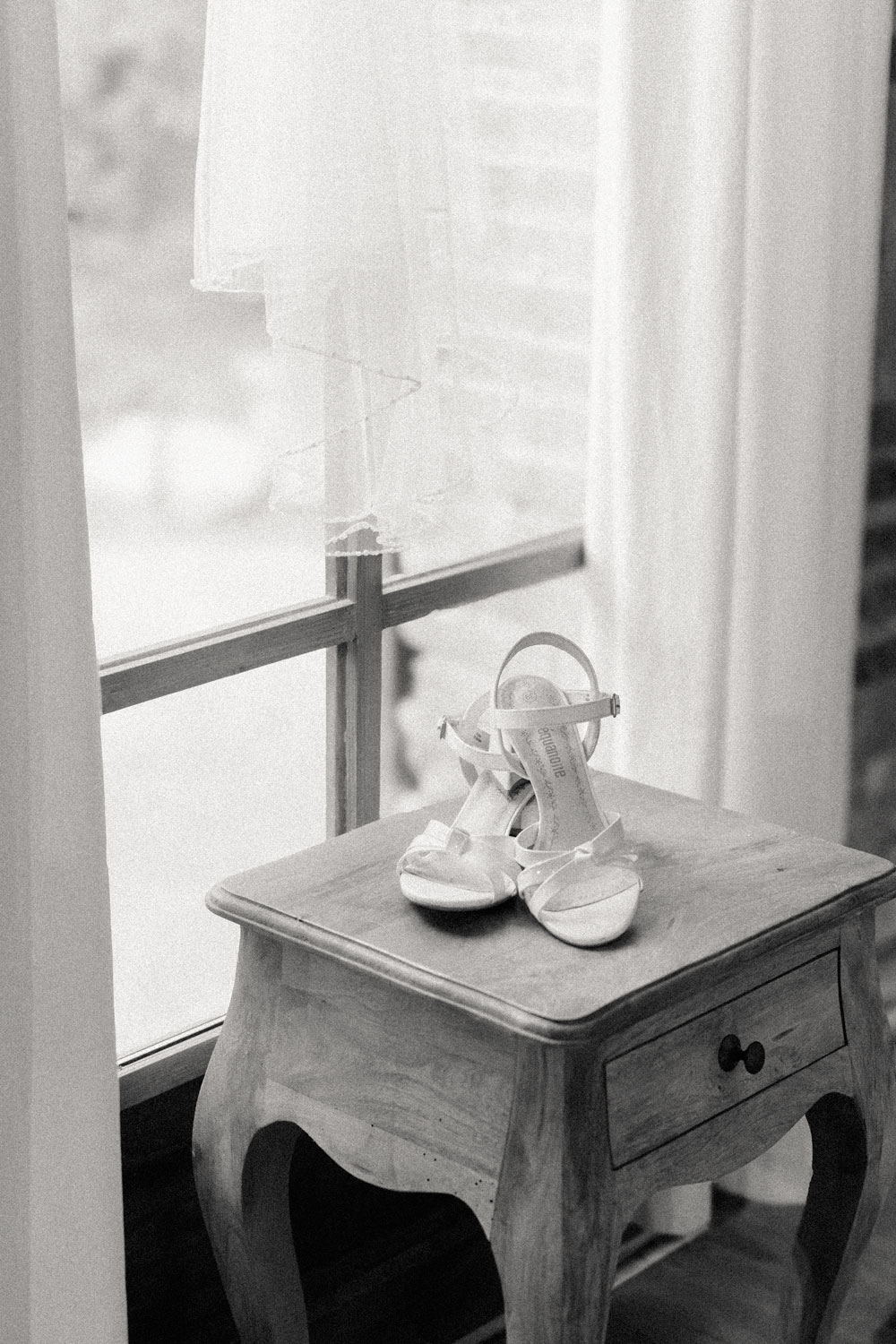 Chaussures blanches de mariée sur un petit tabouret devant une fenêtre – photographe de mariage Pyrénées-Orientales